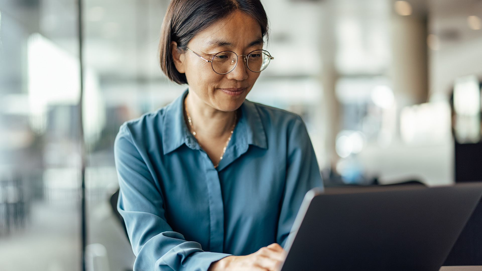 An elderly person using a laptop. The person is wearing glasses and a blue shirt.